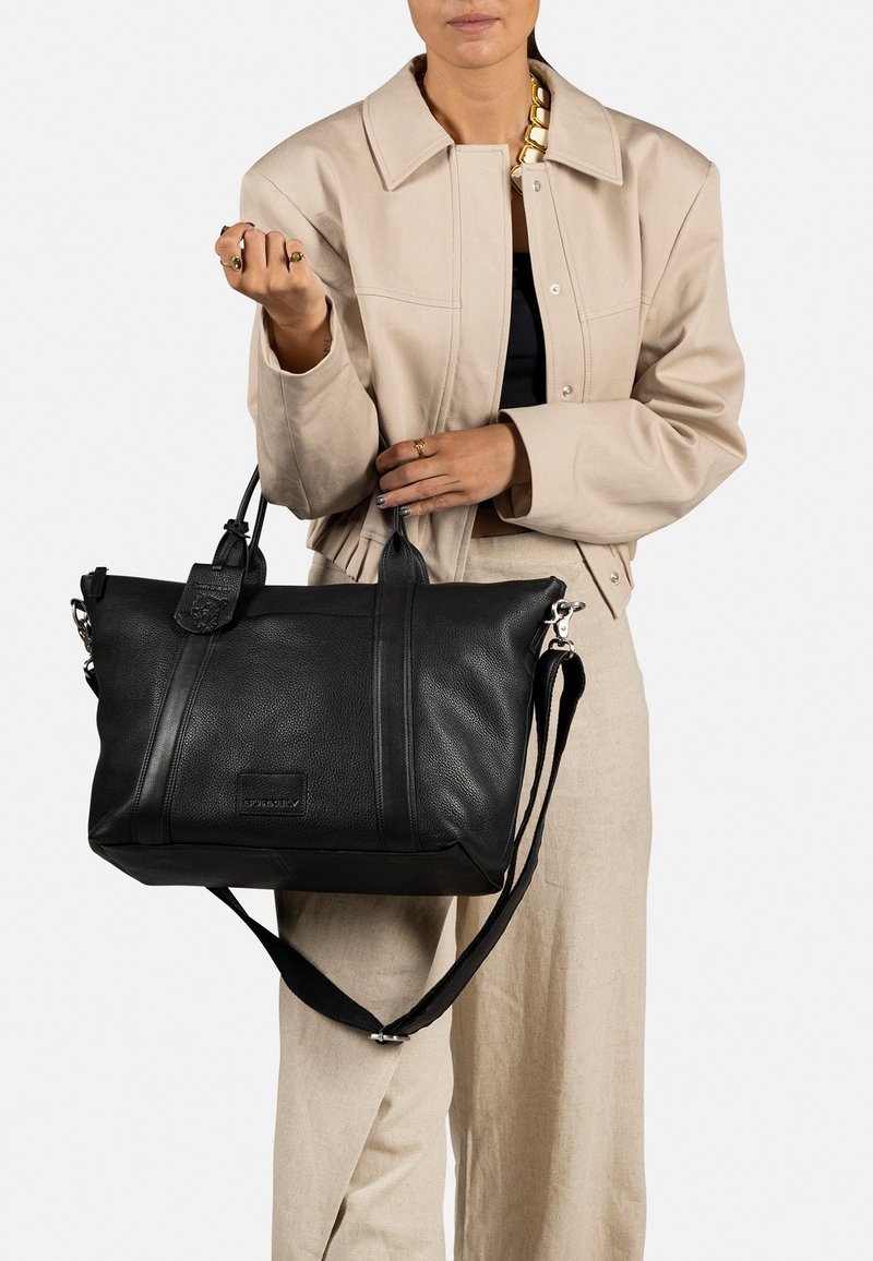 Borsa a mano in pelle nera con finitura testurizzata, manici doppi e tracolla regolabile. Include un caratteristico dettaglio con etichetta e cuciture minime.