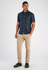 Marineblauw overhemd met korte mouwen en een gladde textuur, gecombineerd met beige slim-fit broeken en zwarte schoenen met een gestructureerd ontwerp.