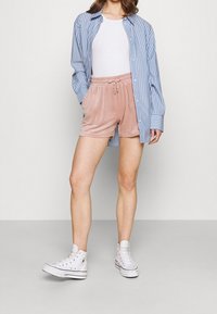 Chemise rayée bleu clair et blanc portée sur un débardeur blanc, assortie à un short en velours rose et des baskets montantes blanches.