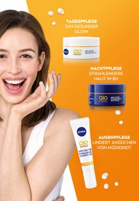 NIVEA Q10 Energy Hautpflegeprodukte ausgestellt: weiße runde Tagescreme, blaue runde Nachtcreme und weiße Tube Augencreme auf orangefarbenem Hintergrund.