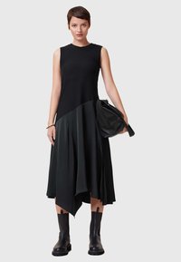 Abito nero al ginocchio con corpino aderente e gonna asimmetrica, realizzato in tessuto liscio. Abbinato a stivali neri alla caviglia e una borsa a spalla.