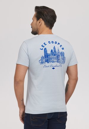 Mężczyzna w jasnoniebieskiej koszulce z niebieskim widokiem Londynu i napisem "LEE COOPER East London E1" na plecach.