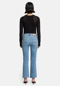 Schwarzes Langarmoberteil, kombiniert mit hellblauen Schlagjeans. Die Jeans haben einen ausgefransten Saum und zwei Gesäßtaschen mit Zickzacknähten.