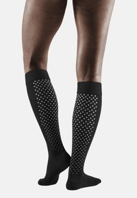 Zwarte knielange sokken met een gestructureerd ontwerp met kleine witte kruisen, geribbelde boorden en een gladde afwerking.