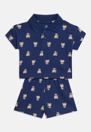Ensemble deux pièces bleu marine pour enfants avec chemise à manches courtes col et short, avec imprimé d’ours en peluche avec des chapeaux bleus et des drapeaux.