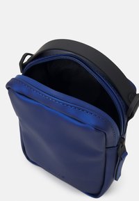 Borsa a tracolla in pelle blu con finitura liscia, apertura superiore con zip e una robusta tracolla nera. Presenta un esterno leggermente imbottito.