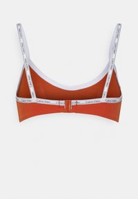 Bralette laranja com acabamento branco, apresentando alças ajustáveis e um fecho de gancho e olho. O material é suave e com ligeiro brilho.