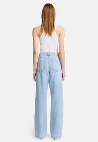 Jeans larges bleu clair avec taille haute, présentant une texture lisse et deux poches arrière, associés à un débardeur blanc.