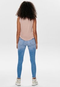 Ljusrosa ärmlös topp kombinerad med blå urtvättade leggings. Leggingsen har en slät yta med sömdetaljer vid bakfickorna.