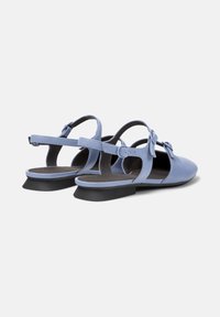 Ljusblå slingback-skor med en liten svart klack och en dekorativ rosett på sidan, som visar en stilren, öppen design.