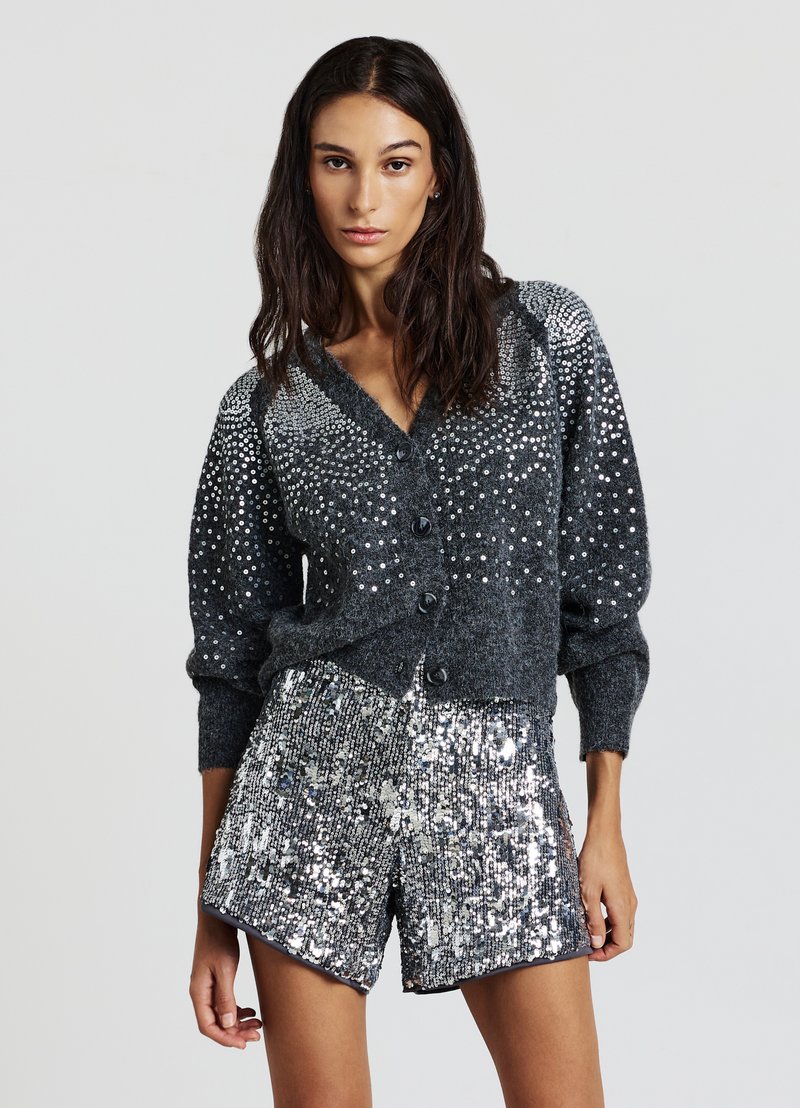 Grauer Cardigan mit silbernen Pailletten, mit V-Ausschnitt, Knopfleiste und Puffärmeln, kombiniert mit glänzenden silbernen Pailletten-Shorts.