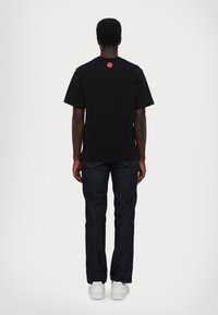 Black short-sleeve t-shirt with a red graphic detail on the back, paired with dark denim jeans and white sneakers.