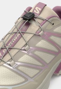 Αξεσουάρ ελαφριάς δομής για τρέξιμο με ανώτερο μέρος από μπεζ και ανοιχτό ροζ πλέγμα, ασφαλές σύστημα κορδονιών και αντανακλαστικές λεπτομέρειες στις πλευρές.