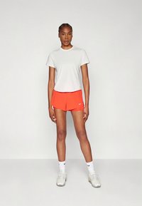 Lysegrå atletisk t-shirt kombineret med lyse orange shorts. Indeholder Nike-logoer, en afslappet pasform og glatte teksturer. Lysegrå sko fuldender outfittet.