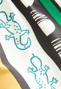 Tissu avec un motif comportant des lézards teal sur un fond blanc, bordé de rayures noires et vertes. Texture lisse, couleurs vives.