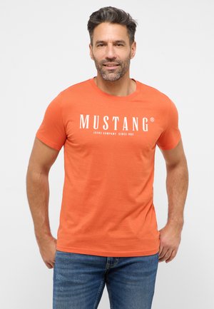 Orange cotton t-shirt with short sleeves, featuring white printed text "MUSTANG JEANS COMPANY SINCE 1932" across the chest.