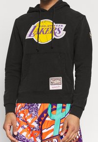 Sweat à capuche noir avec le logo des Los Angeles Lakers en jaune et violet, doté d'une poche kangourou et d'une étiquette portant la mention "Hardwood Classics".