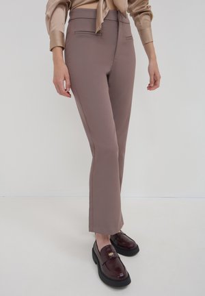 Pantaloni elasticizzati marroni con vestibilità sagomata, dotati di tasche anteriori piatte, vita a media altezza e un leggero svaso all'orlo.