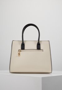 Beige syntetisk handväska med svarta handtag, rektangulär form, en framficka med dragkedja och guldetaljer, samt kontrasterande svarta kanter.