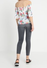 Květinová blůza bez ramen s krátkým rukávem, spárovaná se šedými skinny džíny. Model má na sobě černé sandály. Texturovaná látka s výrazným potiskem.