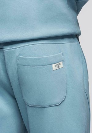 Pantaloni casual azzurri chiari con una tasca posteriore che presenta un'etichetta bianca piccola con testo nell'angolo superiore destro della tasca.