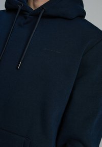 Granatowa bluza z kapturem, wykonana z miękkiego materiału, z kieszenią kangurzą, sznurkami zakończonymi metalowymi końcówkami oraz subtelnym detalem logo.