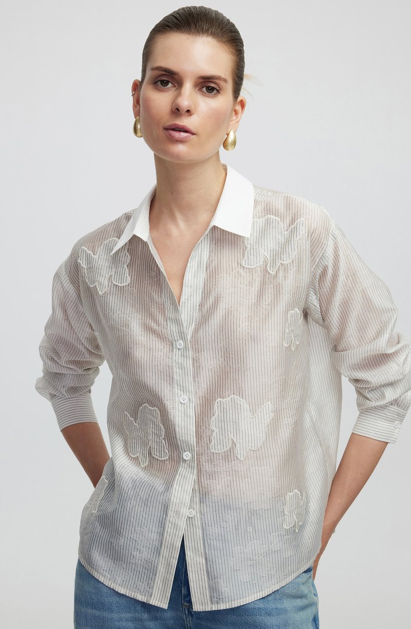 Witte doorschijnende button-up shirt met lichte verticale strepen. Bevat geborduurde bloemenpatronen en een klassieke kraag. Zacht, lichtgewicht stof.