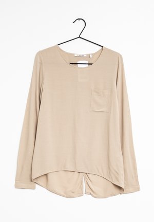 Beige Langarmbluse aus glattem Stoff, mit rundem Halsausschnitt, einer vorderen Tasche und einem geschwungenen Saum mit Seitenschlitzen.