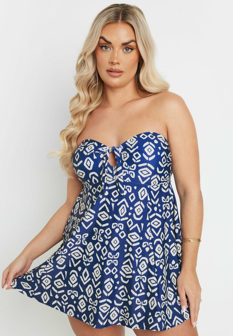 Vestido azul sin tirantes con un lazo en la parte delantera, que presenta un patrón geométrico blanco, falda acampanada y textura de tela suave.
