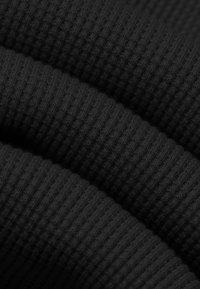 Pieghe di tessuto nero a coste che mostrano una trama a maglia stretta e un motivo rigato diagonale, illuminate da una luce soffusa.