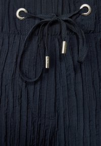 Marint färgad textil med rynkad design, utrustad med dragsko med guldfärgade metalldelar och öglor.