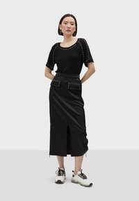 Černý top s krátkými rukávy a ozdobnými hroty, doplněný černou zavinovací sukní s kapsami a předním rozparkem. Vybaven bílými teniskami.