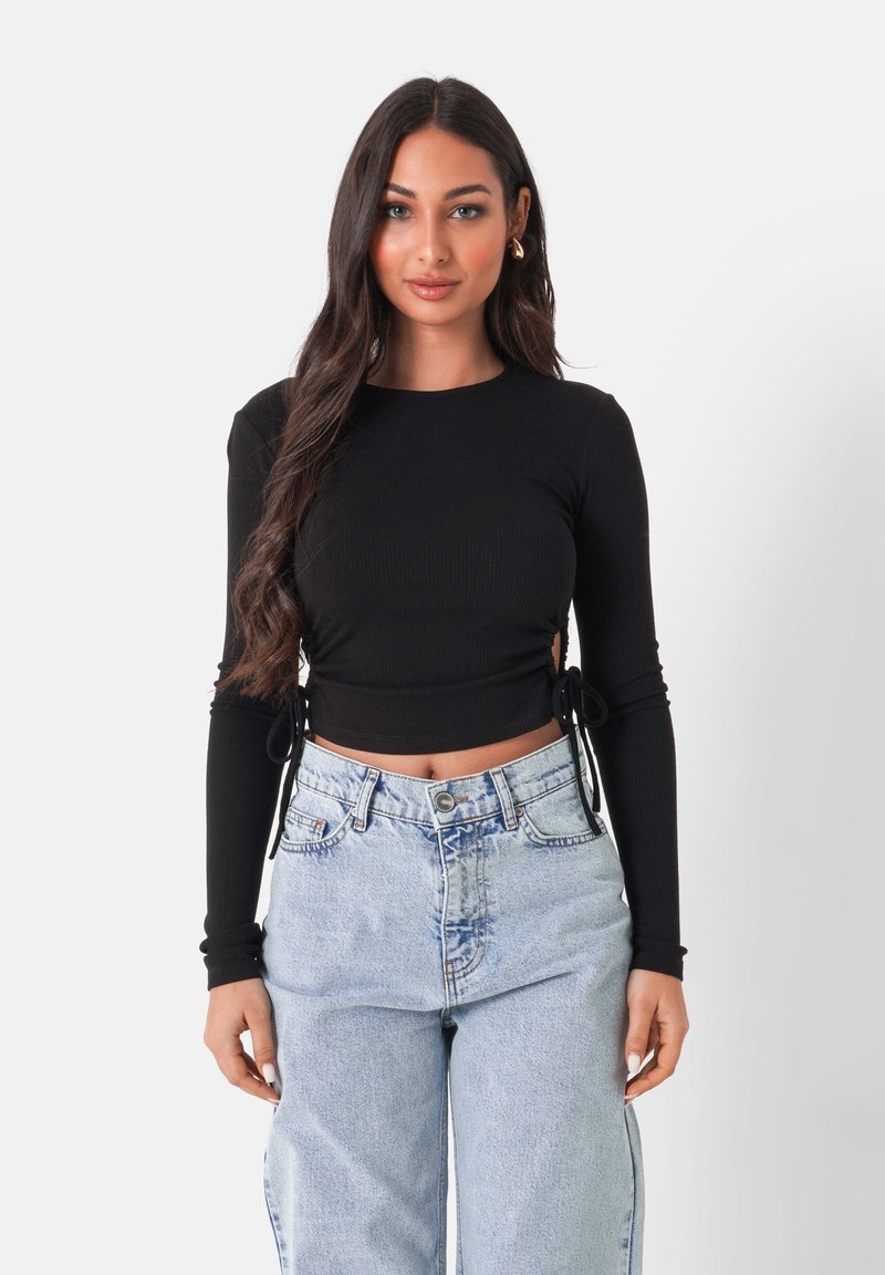 Svart långärmad ribbad kort topp med sidoknytningar, i kombination med högmidjade ljusblå denimjeans. Slät textur, åtsittande design.