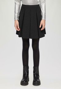 Jupe plissée noire avec des rayures argentées, associée à des collants noirs et des bottes noires à zip mi-mollet, portée avec un haut argenté à manches longues.