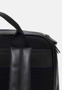 Borsa nera con un pannello in rete testurizzata, dettagli in pelle solida e una maniglia robusta. Chiusura con zip e dettagli di cucitura in contrasto.