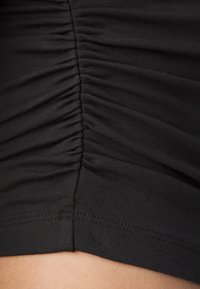 Tela elástica negra con textura fruncida a lo largo de la costura lateral, con un dobladillo suave y un sutil detalle de costura.