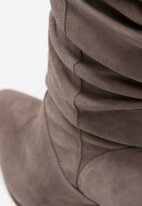 Stivale grigio in suede con un design sbandato, punta affusolata e dettagli di cucitura sottili. Texture liscia con un finish opaco.