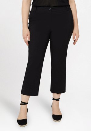 Pantaloni neri a cavallo corto con taglio dritto, dotati di chiusura frontale a bottone e tasche. Indossati con tacchi in stile espadrille neri.