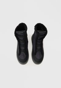 Μαύρες μπότες με πάνω μέρος από μαλακό ύφασμα, αφράτο γιακά και υφασμένο καουτσούκ σόλα. Διαθέτουν φερμουάρ μπροστά και σταυρωτές ιμάντες για ασφαλή εφαρμογή.