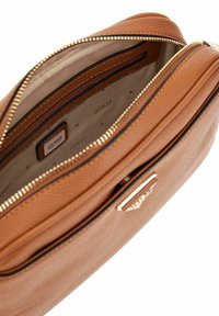 Sac en faux cuir texturé marron avec une fermeture éclair dorée, disposant d'un intérieur spacieux et d'une petite étiquette de marque à l'intérieur.