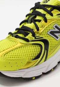 Chaussure de course New Balance jaune vif avec lacets noirs, tissu en mesh et semelle blanche, vue en gros plan.