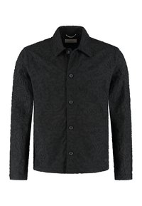 Svart jakke med knapper foran, laget av teksturert stoff med hevede, abstrakte mønstre. Lange ermer og klassisk krage.