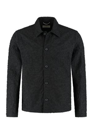 Svart jakke med knapper foran, laget av teksturert stoff med hevede, abstrakte mønstre. Lange ermer og klassisk krage.