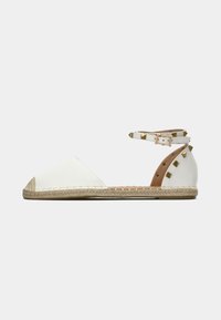 Weiße Espadrille mit spitzem Zehenbereich, Jutesohle und Riemchen am Knöchel, verziert mit goldenen Nieten. Glattes Material mit strukturiertem Fersenbereich.