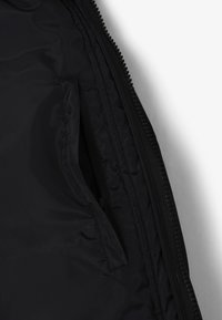 Interior de chaqueta negra con textura suave, que incluye un bolsillo con cremallera y costuras en contraste a lo largo de la línea de la cremallera.