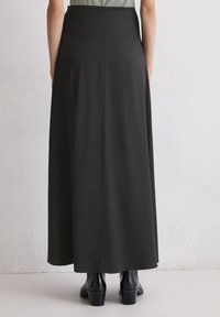 Schwarzer langer Rock mit glatter, matter Oberfläche, der eine gerade Silhouette und eine Rückennaht aufweist, kombiniert mit schwarzen, hohen Stiefeletten.