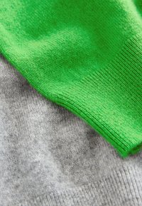 Gros plan d'un tissu tricoté vert et gris avec une texture visible et des bords côtelés qui se superposent.
