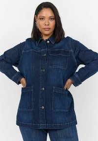 Denim jakna v temno modri barvi z ovratnikom, zapiranjem na gumb, dvema sprednjima žepoma in kontrastnimi šivi. Mehka tekstura.