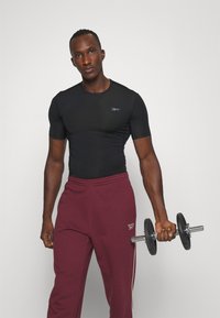 Must have lühikesed varrukad athletic särk; tumepunased treeningpüksid valgete külgtriipudega; hoiab musta hantlit; sile kangas; sobiv disain.