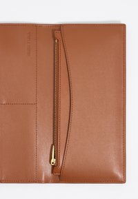 Cartera de cuero marrón claro con una textura suave, que cuenta con un compartimento con cremallera y un logo de la marca en relieve. Incluye ranuras para tarjetas en un lado.